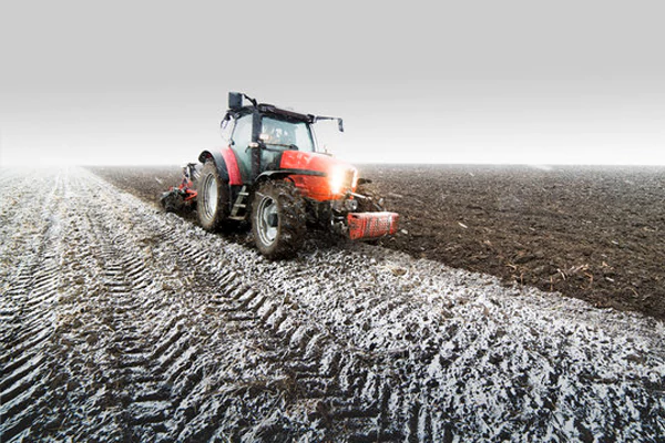 The tractors on the farmland were working in the snow